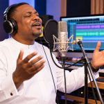 A gospel singer recording worship music in a professional studio with headphones and a microphone.